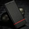 A carbon fiber textured phone case with a red accent stripe and a small embossed logo, placed on a dark, textured surface with a dark sphere in the background. Produktbild-Vorschau