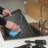 A person is cleaning a grill plate in a sink under running water. Several small pans are visible on the counter. Voir les images du produit