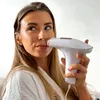 A woman is using a handheld hair removal device on her upper lip. Produktbild-Vorschau