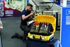 A man is kneeling and working on a tool case in front of a machine. Voir les images du produit