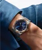 A close-up shot of a man's wrist wearing a blue and rose gold Guess watch, with his arm resting on a blue fabric surface. Produktbild-Vorschau