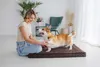A woman is sitting on the floor with her dog, who is standing on a dog bed. Náhľad obrázku produktu