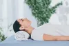 A woman lying on a massage table with a rolled-up towel under her head. Produktbild-Vorschau
