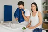 A couple in a bathroom, with the man drying his face with a blue towel. Produktbild-Vorschau