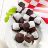 A pile of chocolate-covered peppermint candies on a white plate, with a sprig of mint and a red and white checkered cloth in the background. Produktbild-Vorschau