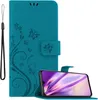 A teal flip phone case with a floral and butterfly design is shown open, with a smartphone inside. A black wrist strap is attached to the side of the case. Náhľad obrázku produktu