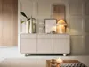 A modern living room setting with a beige sideboard, decorative items, and a lamp. Produktbild-Vorschau