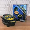 A Batman-themed waffle maker and its packaging are displayed on a wooden surface with a tiled backsplash. Produktbild-Vorschau