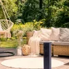 A cozy outdoor patio scene with a wicker sofa, hanging chair, and a dark gray electrical post. Náhled obrázku produktu