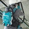 A person wearing a hard hat and a grey shirt is using a Makita backpack vacuum cleaner while working. Náhled obrázku produktu