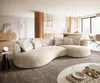 A modern living room with a large, curved beige sofa as the focal point, adjacent to a kitchen area.