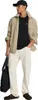 A man wearing a black t-shirt, beige overshirt, and cream pants, holding a black bag. Produktbild-Vorschau