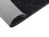 A close-up view of the underside and edge of a black rug, showing the backing material and stitching. Náhled obrázku produktu