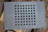 A rectangular cast iron grate with many circular holes is placed on a pile of wood. Náhled obrázku produktu