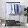 A garment rack with shirts hanging on it, two storage boxes and books on a lower shelf, placed against a textured wall. Náhled obrázku produktu