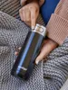 A person holding a black Contigo travel mug while wrapped in a gray knitted blanket. Anteprima dell’immagine prodotto