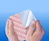 Hands peeling back a layer of a white and red patterned adhesive material against a light blue background. Náhled obrázku produktu