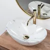 A close-up shot of a marble-patterned vessel sink with a gold faucet, placed on a wooden surface. Anteprima dell’immagine prodotto