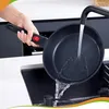 A hand holding a frying pan under running water in a kitchen sink. Produktbild-Vorschau