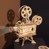 A wooden model of a film projector is displayed on a dark surface with a shadow cast on a brown wall. Produktbild-Vorschau