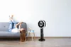 A young woman is lying on a sofa with her legs up, while a fan stands next to a small table with a lamp and a mug. Produktbild-Vorschau