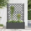 A dark gray planter box with a trellis is filled with white flowers and green plants, set against a white wall with ivy growing on it. Podgląd zdjęcia produktu