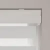 A close-up view of a white roller blind with a cassette headrail, showing the fabric layers and the pull chain. Produktbild-Vorschau