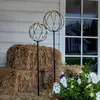 Two LED sphere decorations are placed in front of hay bales, with flowers in the foreground and a house visible in the reflection of a window. Produktbild-Vorschau