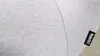 A close-up of a light gray fabric with a black tag that has white text. Produktbild-Vorschau