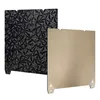 Two 3D printer build plates are shown against a white background. One plate has a black and gray geometric pattern, and the other is a solid gold color. Náhled obrázku produktu