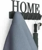 A black metal wall-mounted coat rack with the word 'HOME' cut out, holding a blue fabric item and keys with an umbrella. Náhľad obrázku produktu
