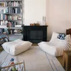 A living room scene with two large, plush white chairs and an ottoman, a black fireplace, and bookshelves. Produktbild-Vorschau