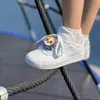 A close-up shot of a child's white sneaker with a cute corgi-themed charm attached to the laces, resting on a thick rope. Produktbild-Vorschau
