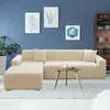 A beige sectional sofa is shown in a living room setting with artwork on the wall and a bookshelf in the background. Náhled obrázku produktu