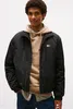 A man wearing a black jacket over a beige hoodie and a checkered shirt. Voir les images du produit