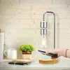 A levitating light bulb is shown on a desk next to a plant and mug, with a hand holding a phone over a wireless charger. Náhled obrázku produktu