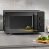 A black Severin microwave oven is shown on a kitchen counter, with broccoli on cutting boards in the foreground and background. Produktbild-Vorschau