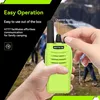 A person's hands are holding a green walkie-talkie, with text overlays describing its features. In the background, a group of people are hiking. Produktbild-Vorschau