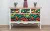 A white dresser with a colorful graffiti-style pattern on the drawers, decorated with two small potted plants and a vase on top. Produktbild-Vorschau