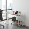 A modern office setting with a large window overlooking a city skyline. A white desk and a rolling cart with office supplies are visible. Voir les images du produit