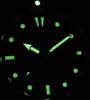 A close-up view of a watch face in the dark, with luminous hands and markers. Produktbild-Vorschau