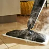 A steam mop is being used on a tiled floor, with steam rising from the mop head. A textured yellow pouf is visible in the background. Podgląd zdjęcia produktu