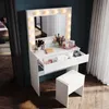 A white vanity table with a mirror and lights, a stool, and makeup items on a wooden floor next to a window with curtains. Voir les images du produit