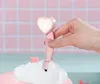A hand is holding a pink heart-shaped shower head with a light on, over a white cloud-shaped bathtub. Produktbild-Vorschau