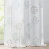 A close-up view of a white sheer curtain with a repeating circular pattern in turquoise and gray. Produktbild-Vorschau