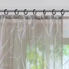 A close-up view of a sheer curtain with a white tree branch pattern hanging from a curtain rod. Produktbild-Vorschau