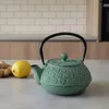 A green cast iron teapot with a black handle sits on a countertop next to a lemon and ginger. Podgląd zdjęcia produktu