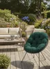 A cozy outdoor seating area with a sofa, coffee table, and a prominent green cushion chair, surrounded by lush garden plants and flowers. Produktbild-Vorschau