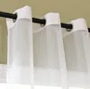 Close-up of white sheer curtains with grommets hanging on a black rod against a light green wall. Produktbild-Vorschau