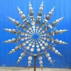 A kinetic wind spinner made of metal, displayed outdoors against a blue wall. Anteprima dell’immagine prodotto